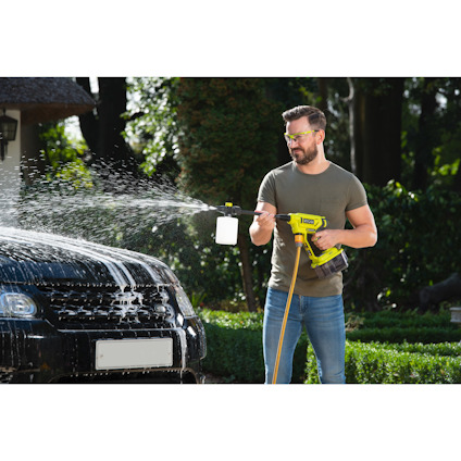 En person i gröna säkerhetsglasögon spolar av en bil med en högtryckstvätt.