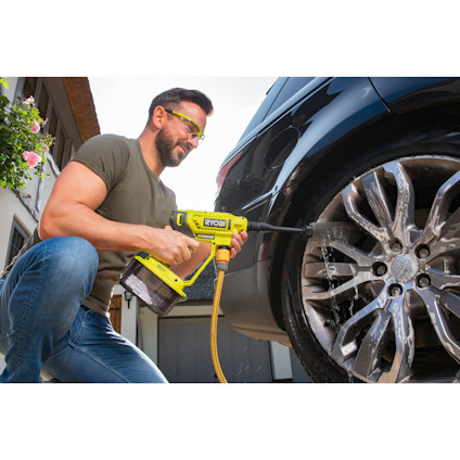 Person använder en grön högtryckstvätt för att rengöra däcket på en bil.