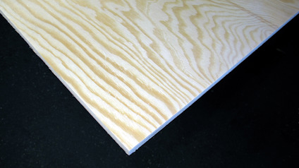 Furuplywoodskiva med ett mönster av ljusa och mörka ringar på en svart bakgrund.