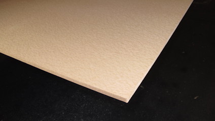 Porös boardskiva i närbild, med ljusbrun yta och synlig kant mot svart bakgrund.