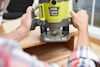 Person som använder en grön och svart Ryobi 1600W handöverfräs på träyta.