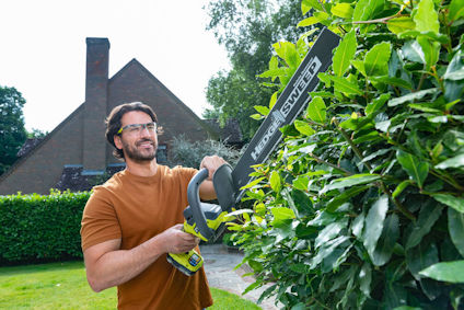 Man klipper buskar med en häcksax i en trädgård.
