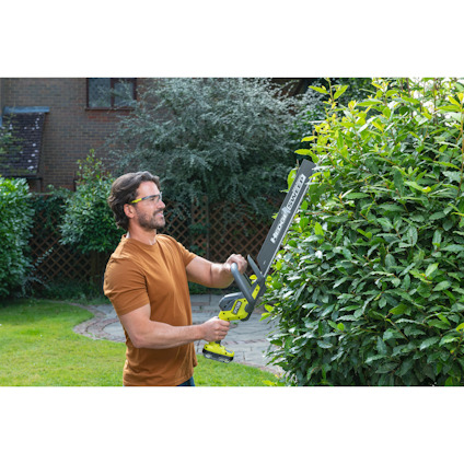 En man klipper en häck med en batteridriven häcksax i trädgården.