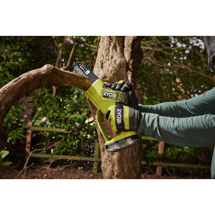 Person använder en grön Ryobi såg för att kapa en gren utomhus.