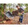 Man with a drill emptying soil from a wheelbarrow supported by trees in a wooded area.