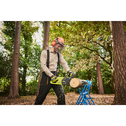 Person använder motorsåg för att såga trästock med skyddsutrustning i skogsmiljö.