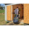 Man pushing a stack of toolboxes on wheels into a wooden shed with open doors.