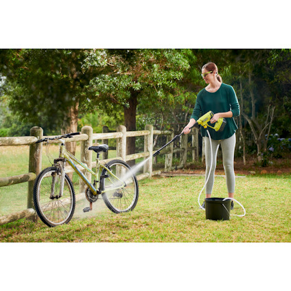 Person som tvättar en cykel med en mellantryckstvätt av märket Ryobi i en grönskande trädgård.