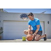 Man i blå t-shirt pumpar en basketboll med en miniluftpump av märket Ryobi nära en garageport, basketkorg syns i bakgrunden.