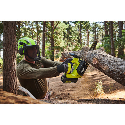 Person med hjälm och skyddsglasögon sågar trädgren med en grön topphandsåg av märket Ryobi i skogsmiljö.