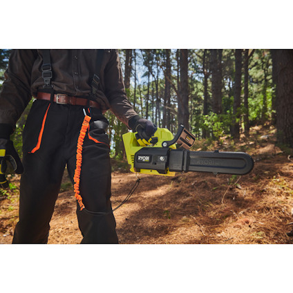 Person håller en grön motorsåg av märket Ryobi i en skog, med ett säkerhetsband fäst vid handtaget.