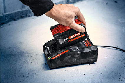 Person placerar ett Bosch Expert 18V-batteri i en laddare på betonggolv.