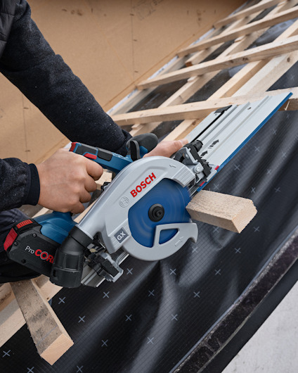 Person använder en Bosch cirkelsåg på en trälist på byggställning.
